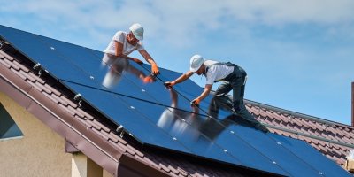 Dva technici instalují solární panely na střechu rodinného domu