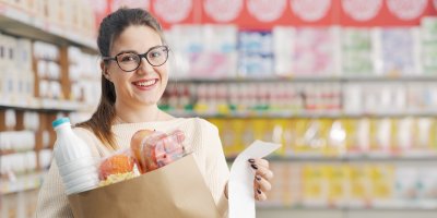 Usmívající se žena s taškou s potravinami a účtenkou v rukou