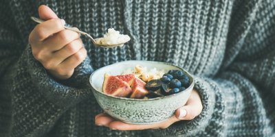 Žena ve svetru jí kaši s ovocem