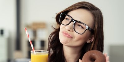 Žena, která drží v rukou sklenici s ovocnou šťávou a donut