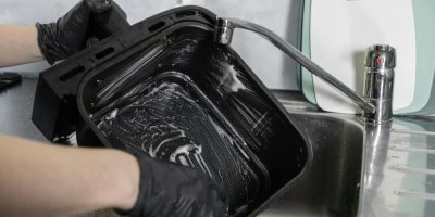 Člověk v černých rukavicích čistí koš olejové fritézy