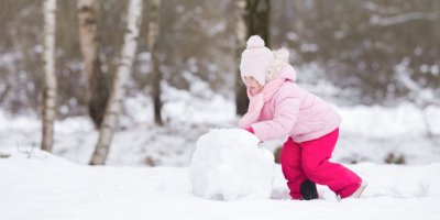Holčička v růžovém zimním oblečení válí sněhovou kouli