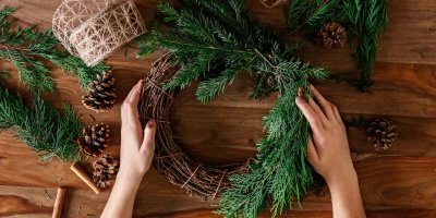 Člověk vyrábí věnec ze slaměného základu, chvojí a šišek