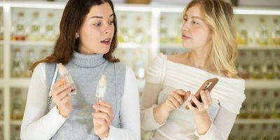 Dvě mladé ženy si vybírají parfémy v obchodě a dívají se na displej telefonu