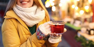 Žena v zimním oblečení drží v rukou horký nápoj ve sklenici