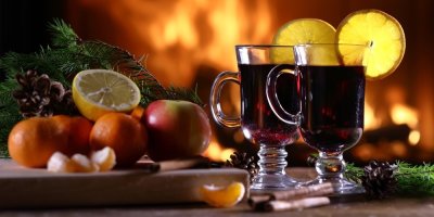 Dva skleněné hrnky svařeného vína, ovoce, v pozadí hořící krb