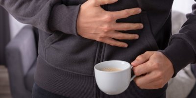 Muž s kávou v ruce si drží ruku na břiše