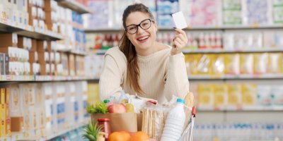 Usmívající se žena v supermarketu s nákupním vozíkem plným potravin a nákupní kartou