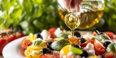 Člověk polévá zeleninový salát olivovým olejem.