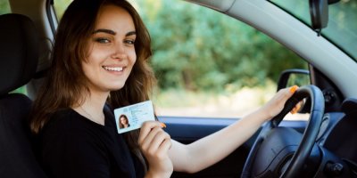 Usmívající se dívka za volantem drží řidičský průkaz