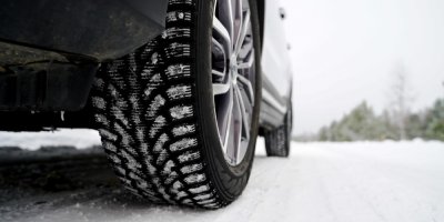 Detail auta se zimními pneumetikami na zasněžené vozovce