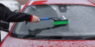 Člověk odstraňuje smetáčkem sníh z čelního skla auta