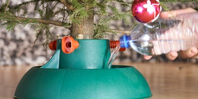 Člověk lije do stojanu vánočního stromečku vodu z PET lahve