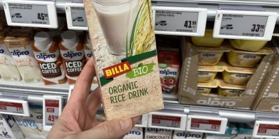 Ruka držící balení rýžového mléka před regálem supermarketu