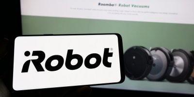 Logo iRobot na displeji telefonu, robotické vysavače na monitoru počítače