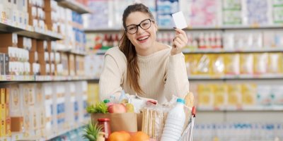 Usmívající se žena v supermarketu s nákupním vozíkem plným potravin a nákupní kartou