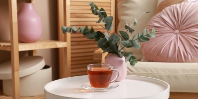 Čaj ve skleněném hrnku a eukalyptus v růžové váze na stolku moderního interiéru