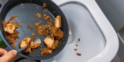 Člověk vyhazuje zbytky jídla z kuchyňské pánve do záchodu