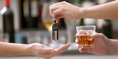 Člověk se skleničkou v ruce podává klíče od auta druhému člověku