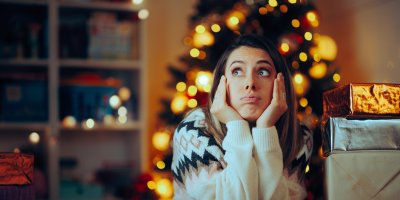 Žena ve stresu sedí před vánočním stromeček, vedle ní jsou zabalené dárky