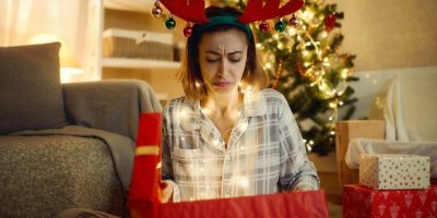 Žena sedící u vánočního stromku je zklamaná z dárku