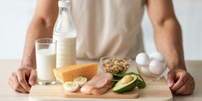 Muž drží na tácu mléko, sýry, maso, avokádo a vejce