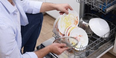 Muž klečí u myčky se špinavým nádobím