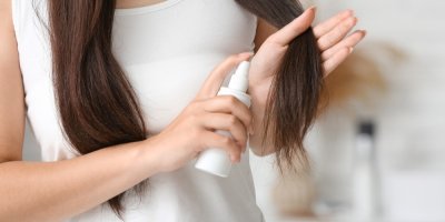 Žena si aplikuje sprej na vlasy