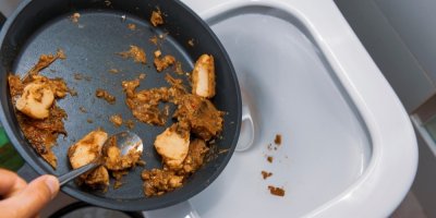 Člověk vyhazuje zbytky jídla z kuchyňské pánve do záchodu