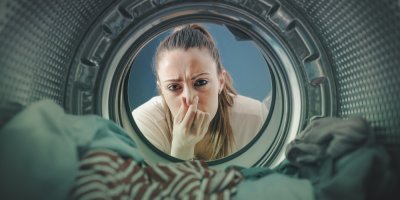 Žena se dívá do pračky s prádlem a drží se za nos