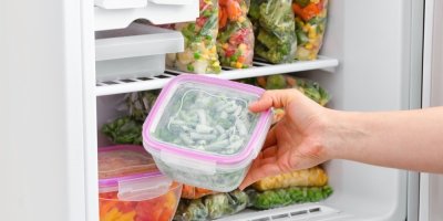 Žena vytahuje mražené fazolové lusky z mrazáku plného mražené zeleniny