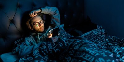 Muž leží v noci v posteli a dívá se do telefonu