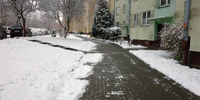 Chodník a zasněžený trávník vedle panelového domu