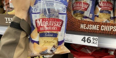 Mužská ruka drží balení brambůrků před regálem v supermarketu
