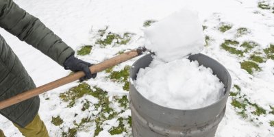 Člověk nabírá lopatou sníh do sudu