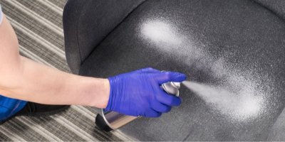 Ruka v rukavici stříká suchou pěnu na čalouněné křeslo.