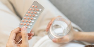 Žena drží v rukou léky a sklenici vody