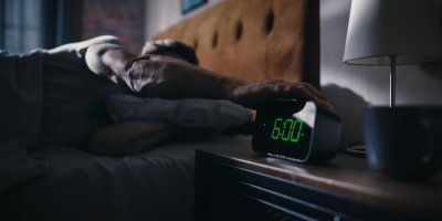 Muž v posteli a budík na nočním stolku ukazující 6 hodin