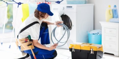 Mladý muž v montérkách s nářadím před pračkou