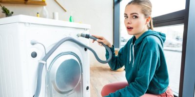 Žena dřepí ze zadní strany pračky a drží hadici