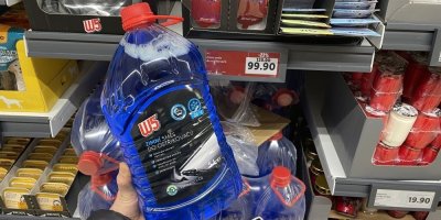 Ruka držící kanystr zimní směsi do ostřikovačů před regálem supermarketu