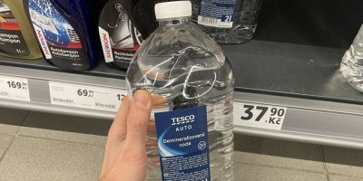 Ruka držící kanystr demineralizované vody před regálem supermarketu