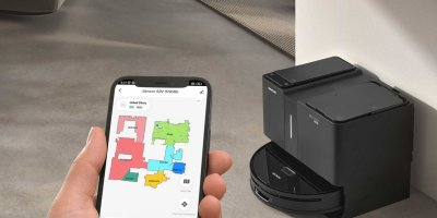 Mobil v rukou a v pozadí robotický vysavač