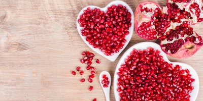 Rozkrojené granátové jablko a zrníčka granátového jablka v miskách ve tvaru srdce