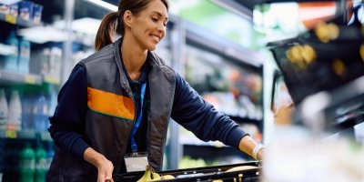 Usmívající se zaměstnankyně supermarketu drží přepravku banánů