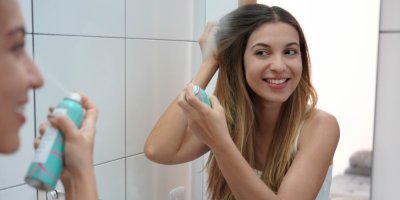 Mladá žena si před zrcadlem aplikuje suchý šampon na vlasy