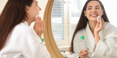 Žena si před zrcadlem čistí pleť micelární vodou