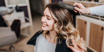 Žena s vlnitými vlasy se směje a někdo ji češe