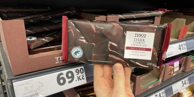 Ruka držící tabulkovou čokoládu před regálem supermarketu