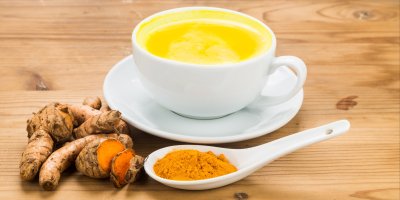 Kurkumový čaj v šálku, mletá kurkuma na lžičce, oddenek kurkumy